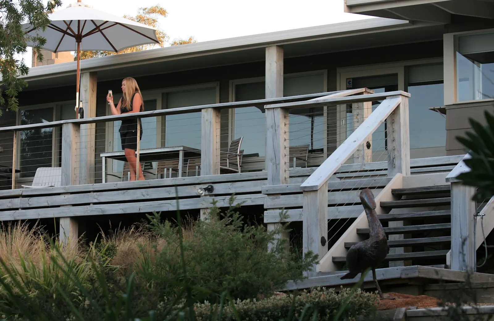 Guest with a glass of sparkling wine on the north-facing deck under a market umbrella at The Waterfront Loch Sport
