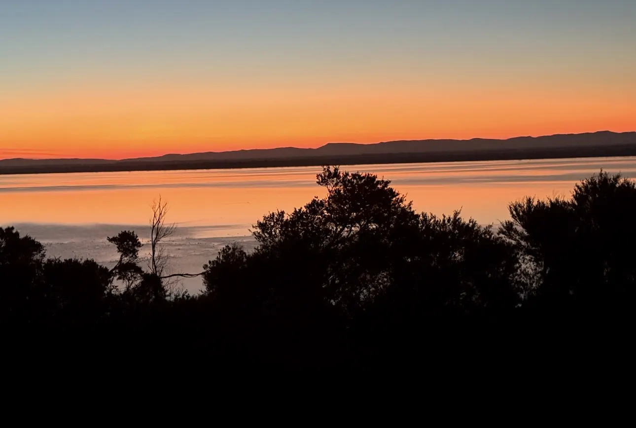 Orange dusk sky reflected in the still water of Lake Victoria with the mountains beyond